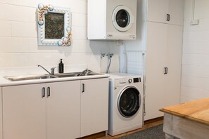 Une petite buanderie équipée d’un lave-linge, d’un évier et de placards.
