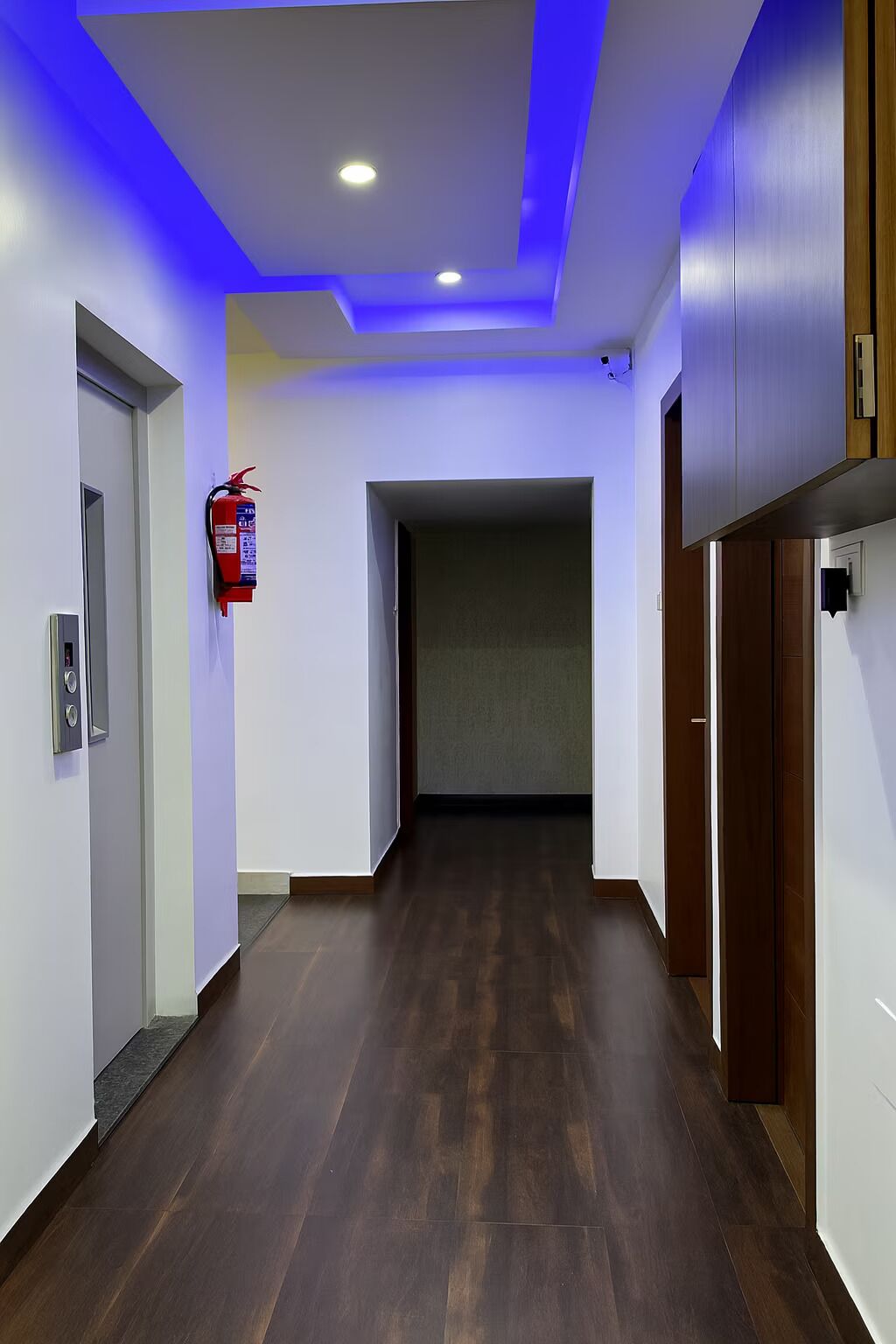 A hallway with wooden flooring, white walls, and blue ceiling lighting.
