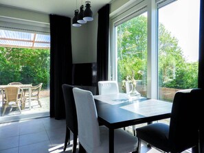 A dining area with a table and chairs, a vase with flowers, and a view of greenery outside. - Quiet Zeeland Base With Pool (Oostkapelle)