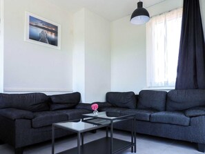 A modern living room with a dark grey sofa set, a glass coffee table, and a pendant light. - Quiet Zeeland Base With Pool (Oostkapelle)