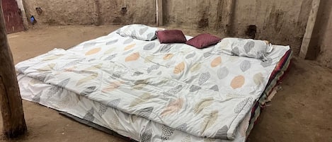 A bed with a patterned bedspread and pillows in a room with a concrete floor and walls.