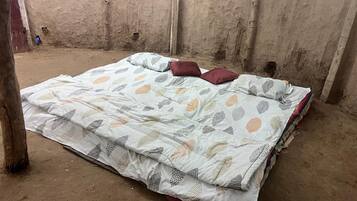 A single bed with a patterned bedspread in a room with concrete walls and a dirt floor.