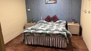 Un dormitori amb un llit, dues taules de nit, un ventilador fixat a la paret i un quadre amb marc.