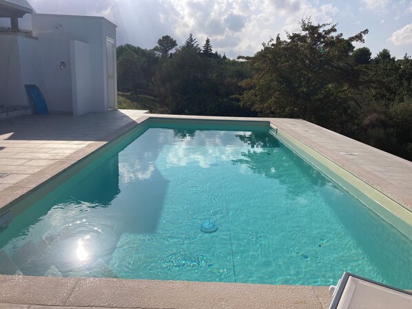 Ein rechteckiger Pool mit klarem Wasser, umgeben von einer gefliesten Terrasse.