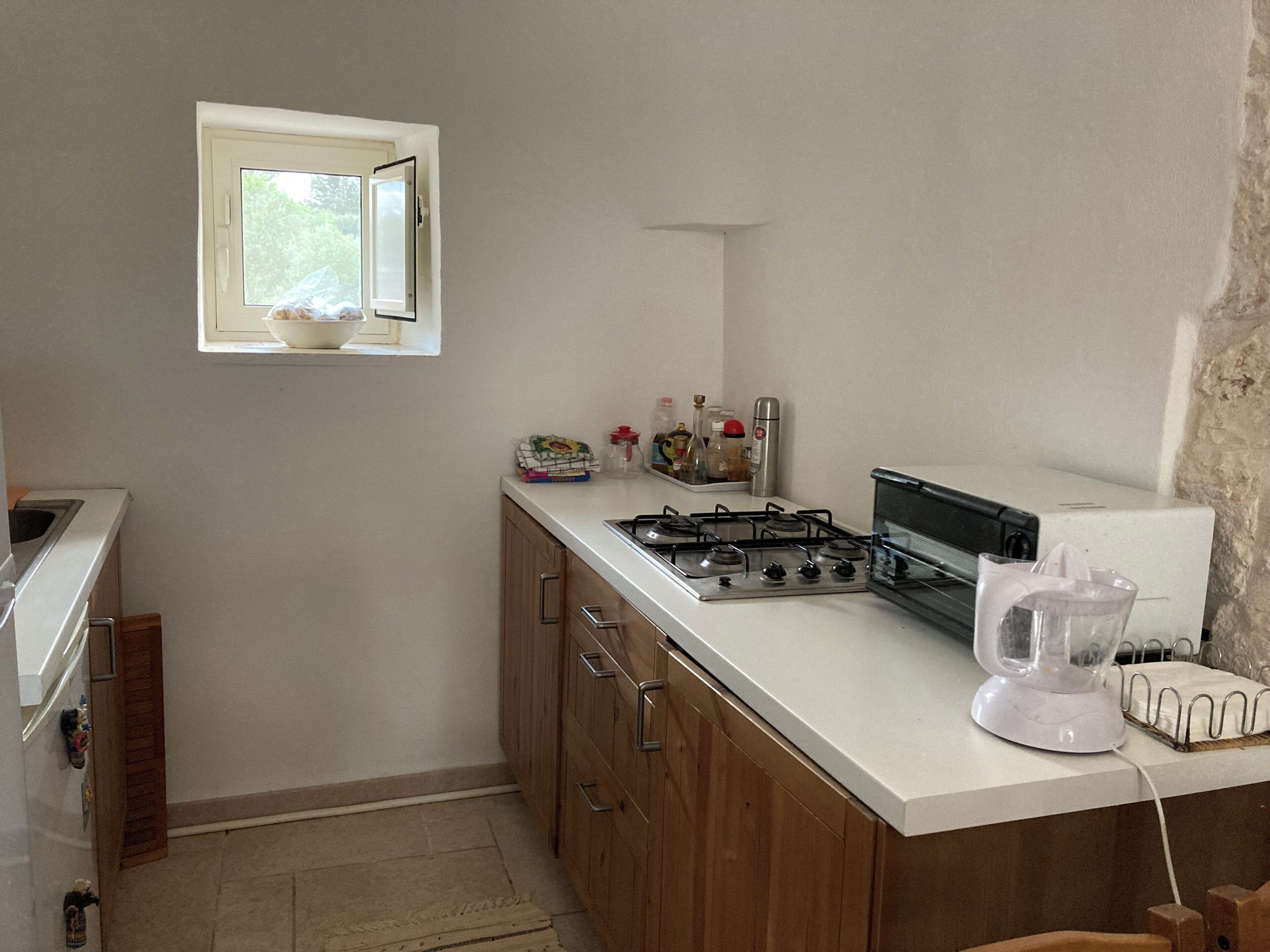 Une cuisine de taille réduite, équipée d’une cuisinière à gaz, d’une petite fenêtre et de meubles de rangement en bois.