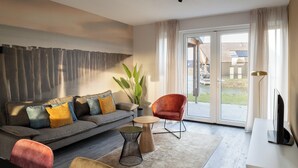 Ein modernes Wohnzimmer mit einem grauen Sofa, einem roten Sessel, einem kleinen runden Tisch und einem Fernseher auf einer weißen Kommode.