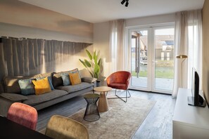 Ein modernes Wohnzimmer mit einem grauen Sofa, einem roten Sessel, einem kleinen runden Tisch und einem Fernseher auf einer weißen Kommode.