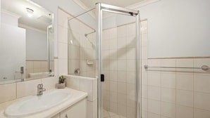 A bathroom with a glass-enclosed shower, a sink, and a mirror. - Belle Escapes - Bayview Escape Glenelg (Holdfast Bay)