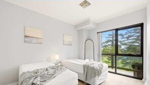 A room with two beds, a large window, and a view of trees. - Belle Escapes - Bayview Escape Glenelg (Holdfast Bay)