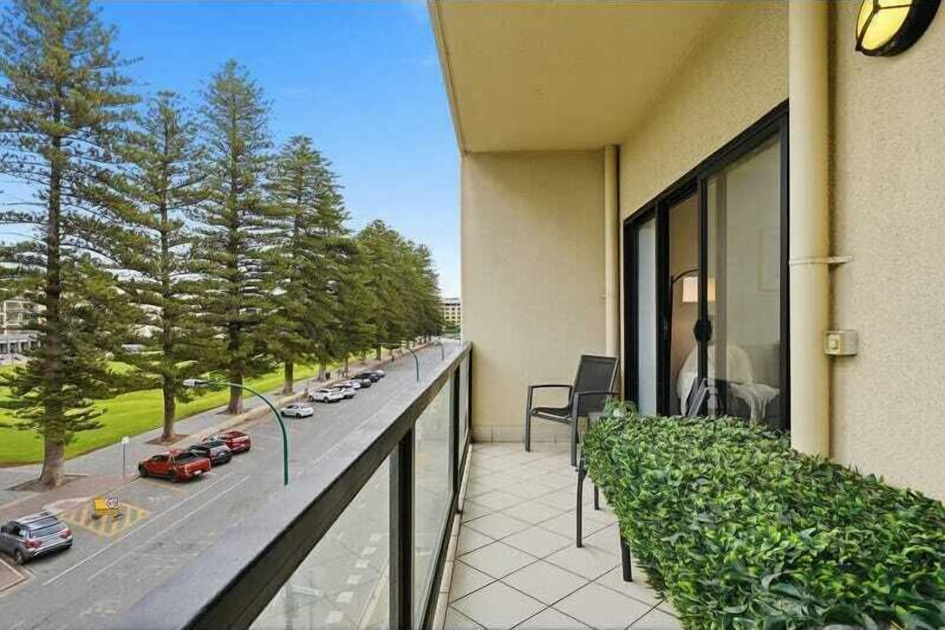 Un balcon donnant sur une rue bordée d’arbres, avec une chaise et une petite table.
