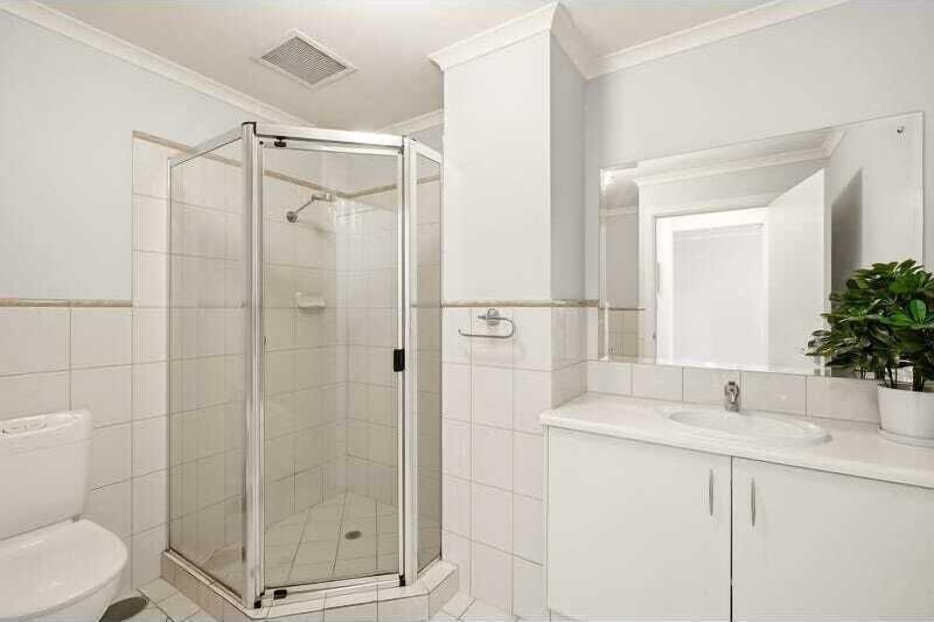 A bathroom with a glass-enclosed shower, a white sink, and a mirror above it.