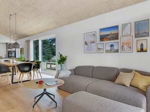 Ein modernes Wohnzimmer mit einem grauen Sofa, einem runden Couchtisch und einem Essbereich mit Tisch und Stühlen.