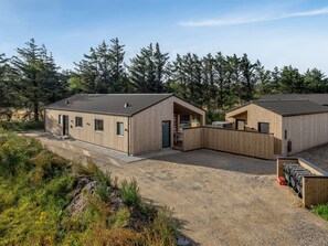 Eine moderne Holzblockhütte mit einem Schotterweg und Wald im Hintergrund.