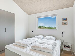 Quarto com uma cama, janela com vista para o verde e uma mesinha com livros.