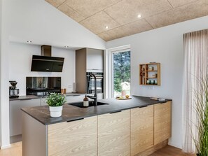 Eine moderne Küche mit einer zentralen Kochinsel, eingebauten Geräten und einem großen Fenster für natürliches Licht.