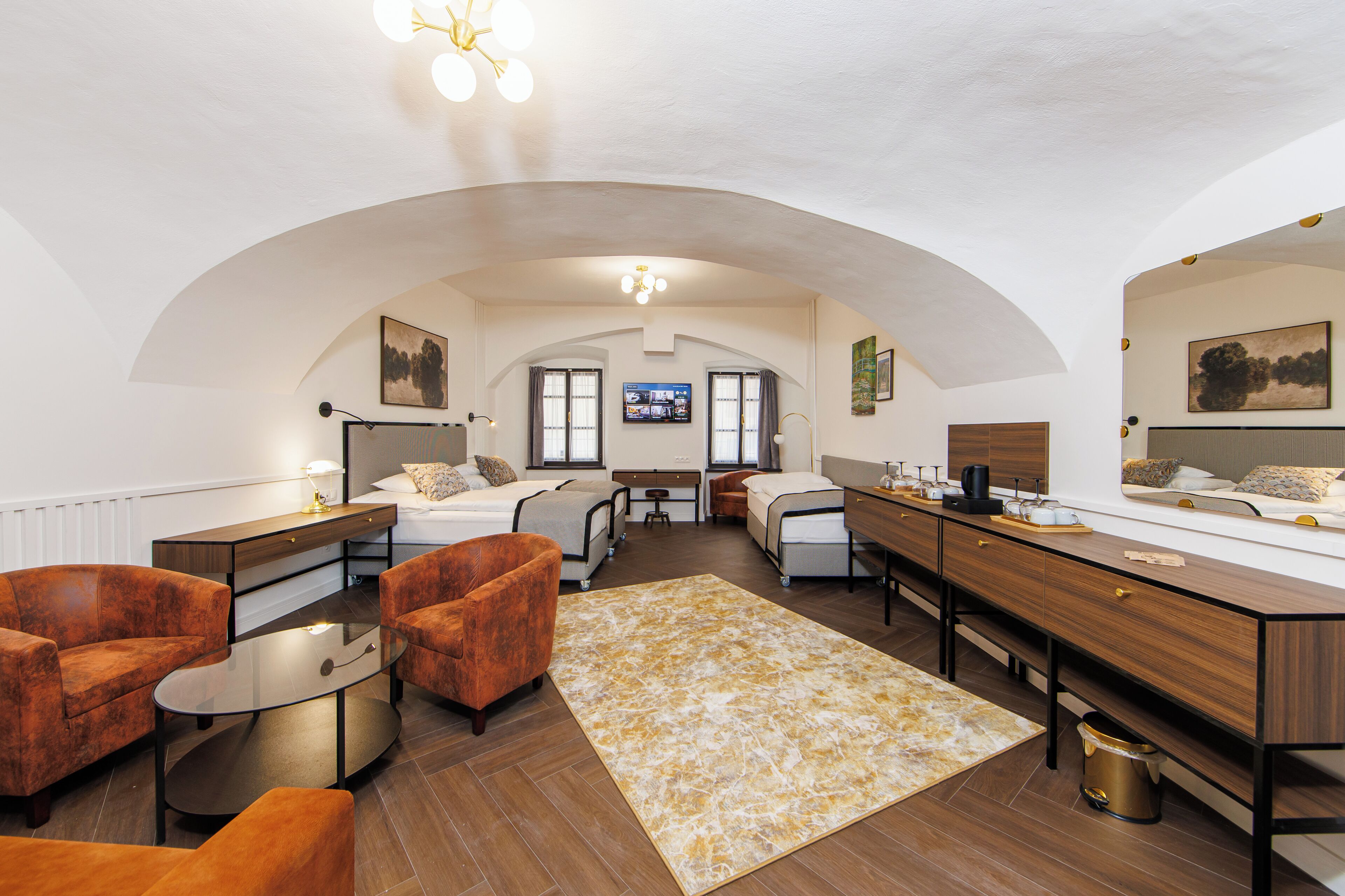 A modern hotel room with a curved ceiling, a bed, a desk, a chair, and a television.