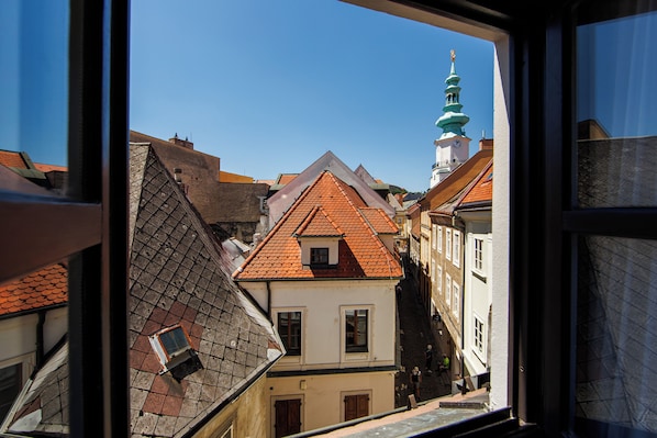 A view of a building with a red-tiled roof and a green spire, seen through a window. - APLEND Paul Inn (Bratislava)