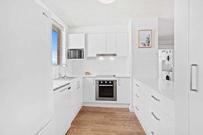A modern kitchen with white cabinetry, a built-in oven, and a microwave. - Escape on the Esplanade (Gold Coast)