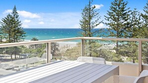 A balcony with a table and chairs, overlooking a beach and ocean. - Escape on the Esplanade (Gold Coast)