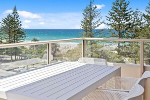 A balcony with a table and chairs, overlooking a beach and ocean. - Escape on the Esplanade (Gold Coast)