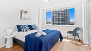 A hotel room with a bed, a chair, a window with a view of a building, and a ceiling fan. - Escape on the Esplanade (Gold Coast)