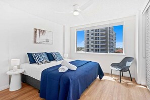 A hotel room with a bed, a chair, a window with a view of a building, and a ceiling fan. - Escape on the Esplanade (Gold Coast)