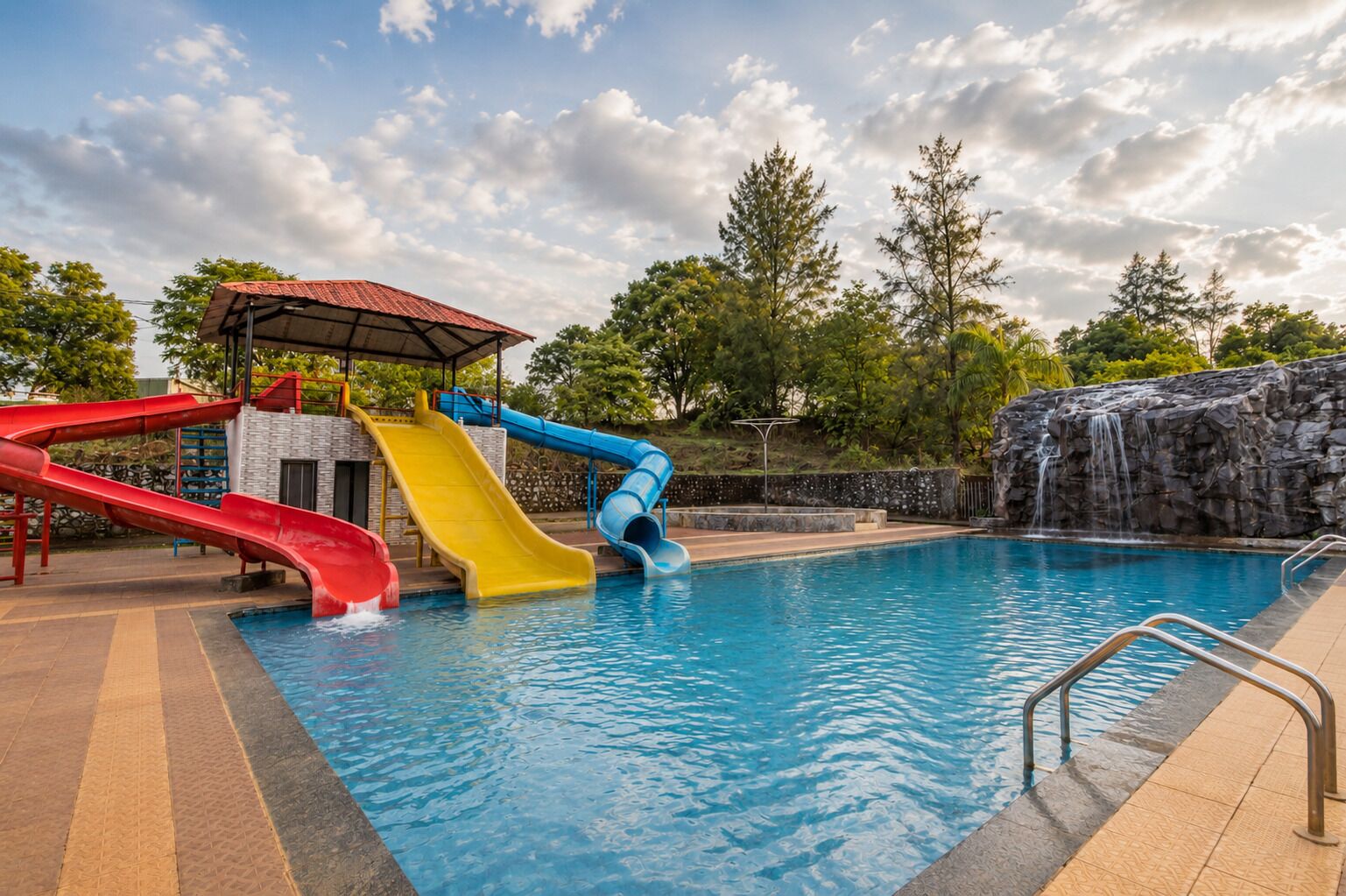 A swimming pool with multiple slides, a covered area, and a rocky waterfall feature.