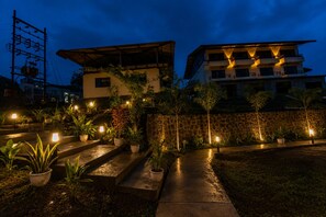 Vista nocturna de un edificio con varios pisos, escaleras exteriores y plantas en macetas.