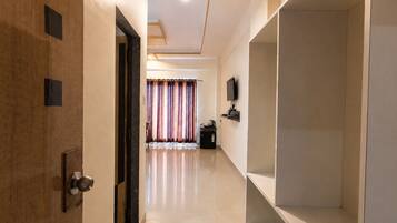 A hotel corridor with a wooden door, a flat-screen TV mounted on the wall, and a tiled floor.