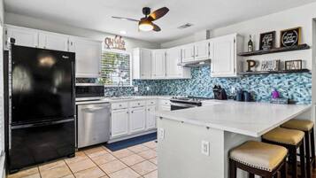 A kitchen with white cabinets, a black refrigerator, a backsplash with blue tiles, and a ceiling fan.