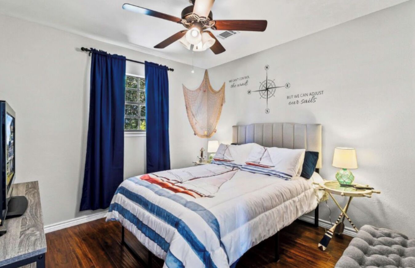 Un dormitorio con cama, ventilador de techo, mesita de noche con lámpara y un diseño de brújula en la pared.
