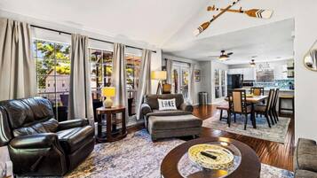Ein geräumiges Wohnzimmer mit einer Ledersofa, einem Hocker und einem Couchtisch. Es gibt einen Essbereich mit Tisch und Stühlen, und im Hintergrund eine Küche.