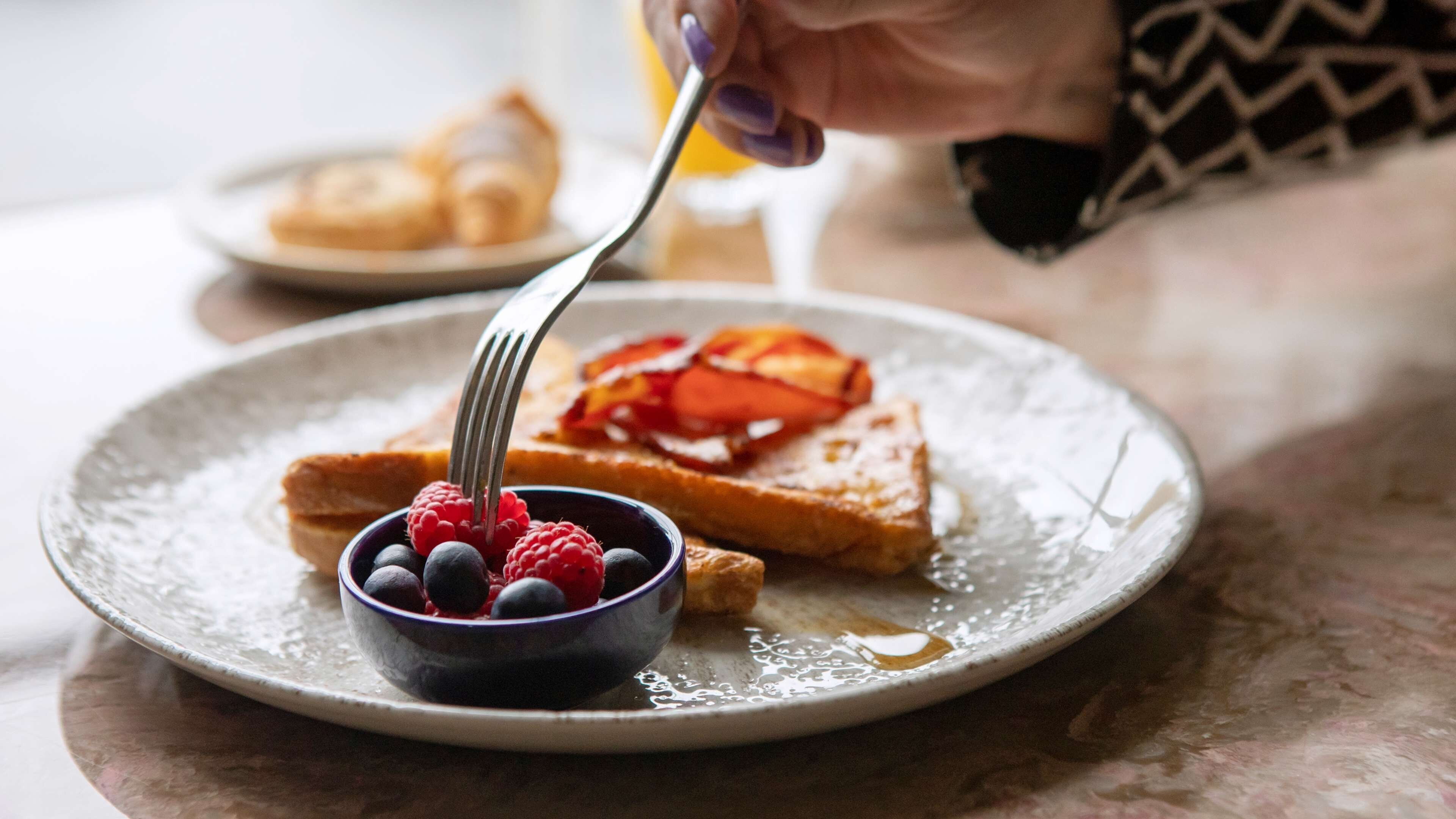 Ein Teller mit Toast, Beeren und einem Löffel.