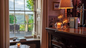 A bar area with a view of greenery outside, a candle on the windowsill, and a book titled 'The Drunken Botanist' on the counter. - Burleigh Court Cotswolds (Stroud)