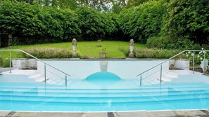 A swimming pool with a stone border, surrounded by lush greenery and a stone wall. - Burleigh Court Cotswolds (Stroud)