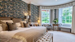 A bedroom with a large bed, a bench, a window seat, and a view of greenery outside. - Burleigh Court Cotswolds (Stroud)