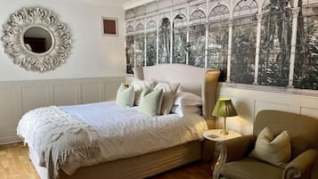 A bedroom with a large bed, a round mirror, a green lamp, and a view through a window with a decorative frame.