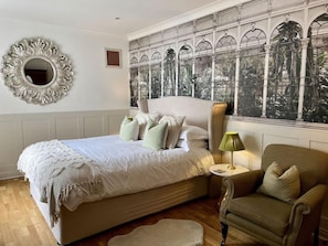 Een slaapkamer met een groot bed, een ronde spiegel, een groene lamp en een uitzicht door een raam met decoratieve lijst.