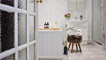 A bathroom with a white vanity, a glass shower enclosure, and a bottle of champagne on a stool.