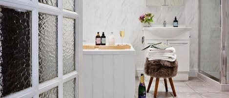 A bathroom with a white vanity, a glass shower enclosure, and a bottle of champagne on a stool.