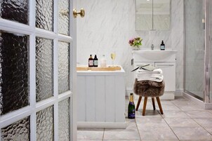Un baño con tocador blanco, cabina de ducha de vidrio y una botella de champán sobre un taburete.