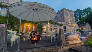 An outdoor seating area with a fire pit, a large umbrella, and stone sculptures. - Burleigh Court Cotswolds (Stroud)