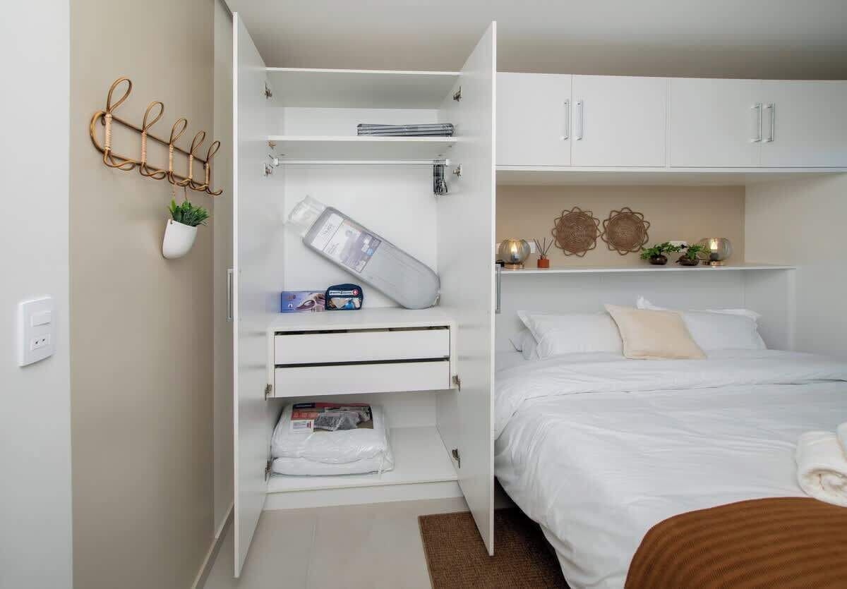 Un dormitorio con una cama, un armario blanco, una planta colgante y un estante en la pared.