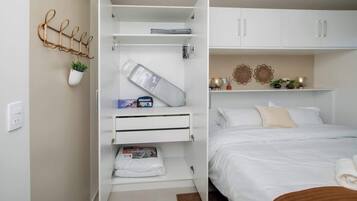Un dormitorio con una cama, un armario blanco, una planta colgante y un estante en la pared.