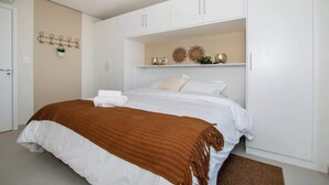 A bedroom with a bed, white cabinets, a wall-mounted plant, and decorative items. - Corporate Stays First Living - 702 (Asunción)