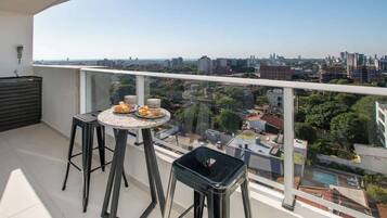 Un balcón con una mesa, dos taburetes y vistas a un paisaje urbano.