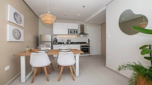 A modern kitchen with white cabinetry, a microwave, and a stove. There is a dining area with a wooden table and white chairs. - Corporate Stays First Living - 702 (Asunción)