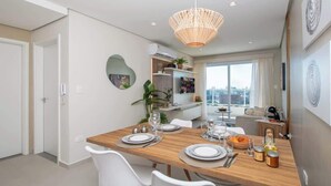 A modern dining area with a wooden table set for four, white chairs, a hanging light fixture, and a city view through large windows. - Corporate Stays First Living - 702 (Asunción)