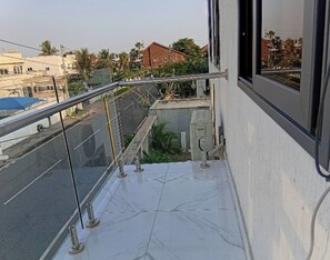 A balcony with a glass railing, a tiled floor, and a view of a street with buildings and trees. - BGG Havens (Accra)