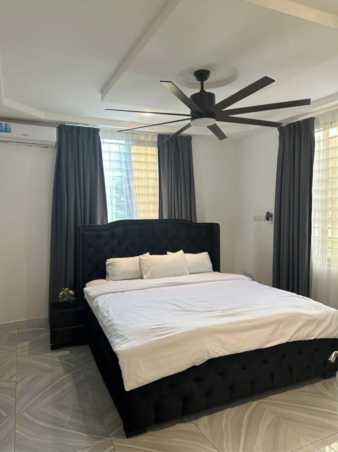 A bedroom with a bed, a ceiling fan, and a window with curtains.